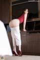 A woman in a red top and white skirt bending over a kitchen counter.