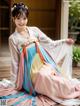 A woman in a colorful hanbok sitting on a wooden floor.