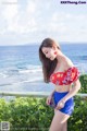 A woman in a red top and blue shorts posing by the ocean.