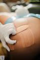 A person in white gloves is putting a bandage on a woman's thigh.