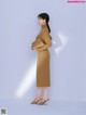 A woman in a brown dress standing in front of a white wall.