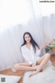 A woman sitting on a white rug in front of a window.