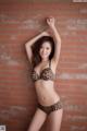 A woman in a leopard print bikini posing in front of a brick wall.