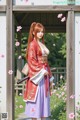 A woman in traditional attire stands in a garden with cherry blossoms.