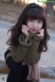 A young woman sitting on a wooden bench with her hand on her chin.