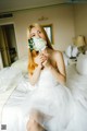 A woman in a white dress sitting on a bed holding a flower.