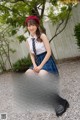 A young woman in a school uniform sitting on a suitcase.