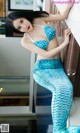 A woman in a blue mermaid costume leaning against a wall.